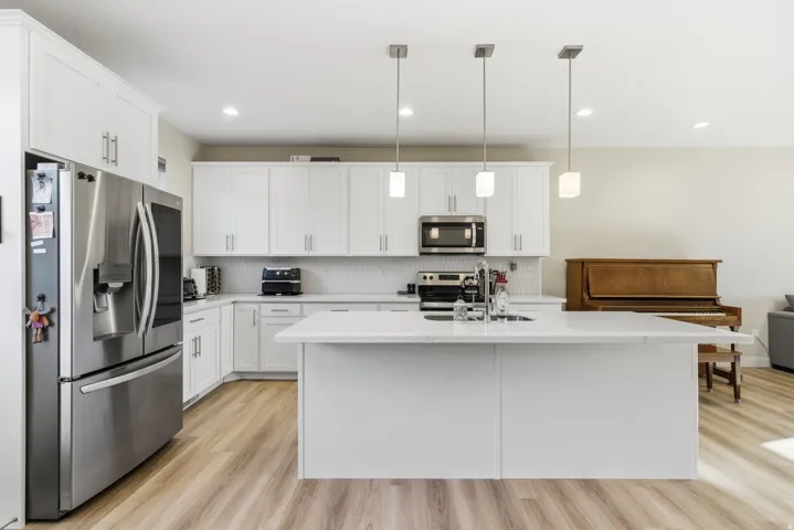 White shaker-style cabinetry, stainless steel appliances, light wood-finish flooring, white countertop, and recessed ceiling lighting