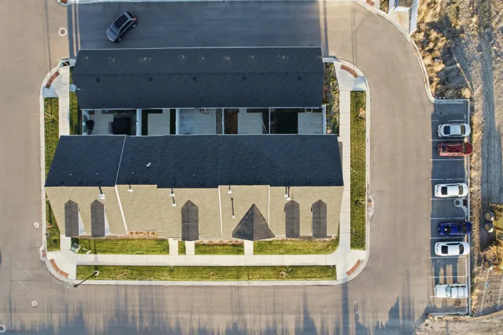 Townhome complex with dark shingle roofing, light-colored exterior siding, and individual patio spaces