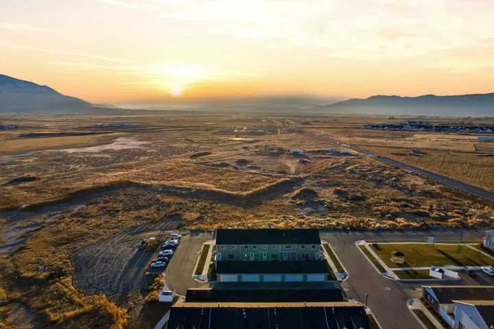 Aerial perspective showcasing a multi-unit property with a paved parking area and individual garage access, set against a backdrop of distant mountains