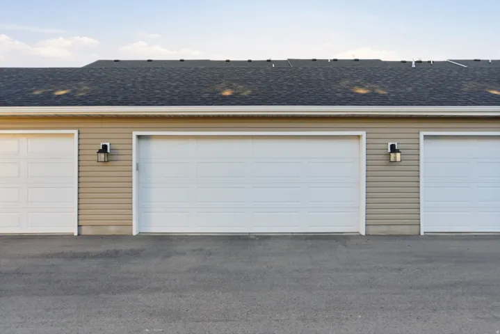 Multiple garage doors with paneling, exterior wall sconces, asphalt driveway, and shingled roof