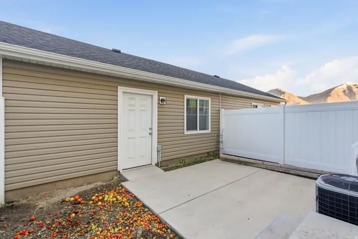 Concrete patio with a white privacy fence, exterior door, and a single window set into tan siding