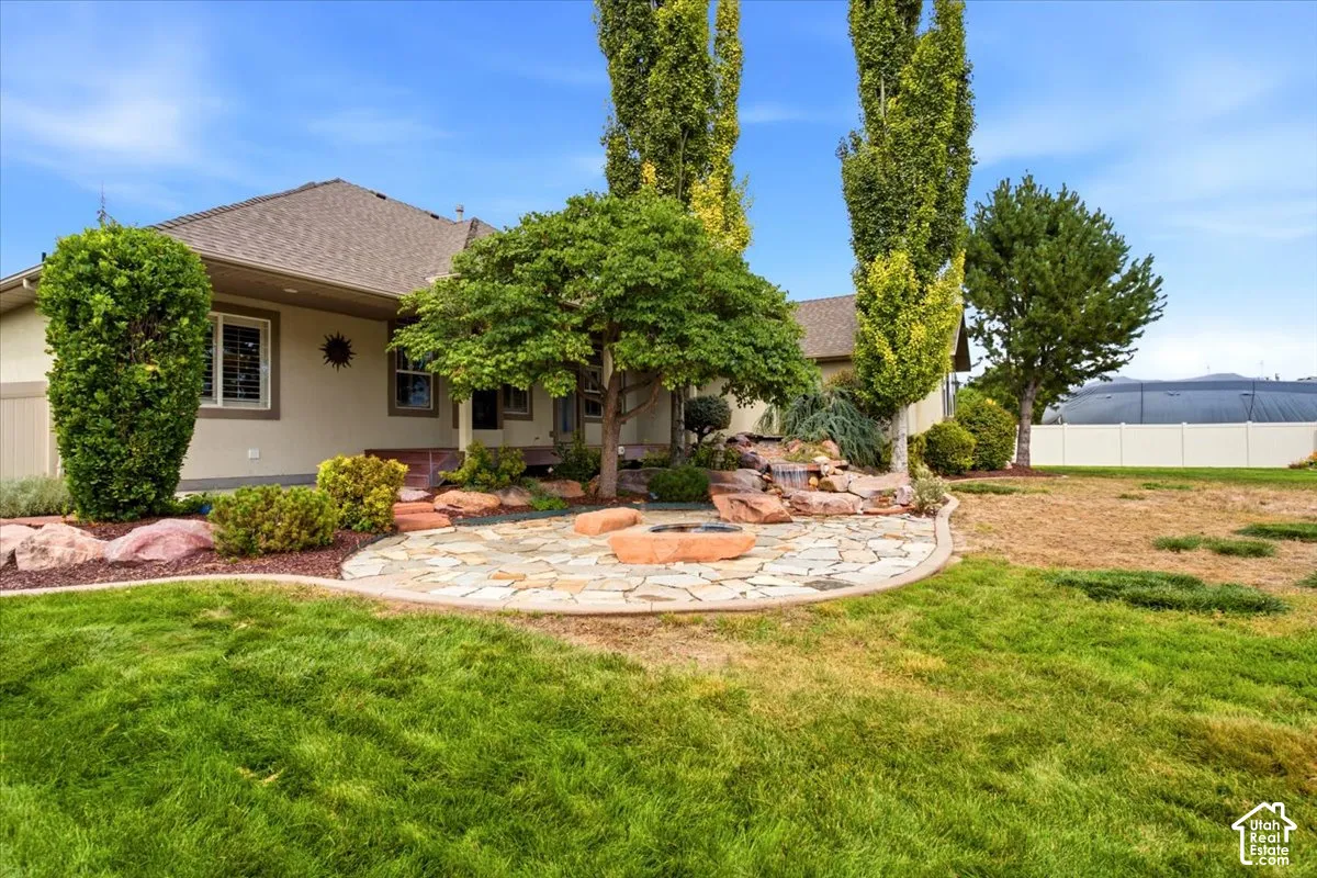 Stone patio with built-in fire pit, mature landscaping with ornamental trees, and a rock waterfall feature