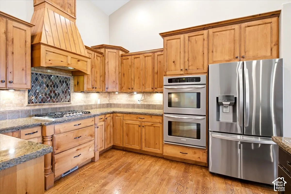 Kitchen featuring wood cabinetry, stainless steel appliances, granite countertops, and wood-finish flooring