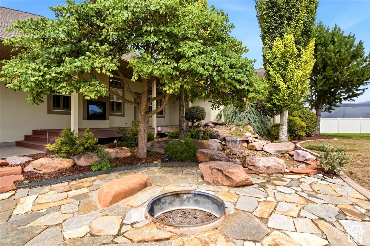 Irregular flagstone patio featuring an integrated fire pit, expansive rock landscaping with a water feature, mature trees, and a covered patio area with steps