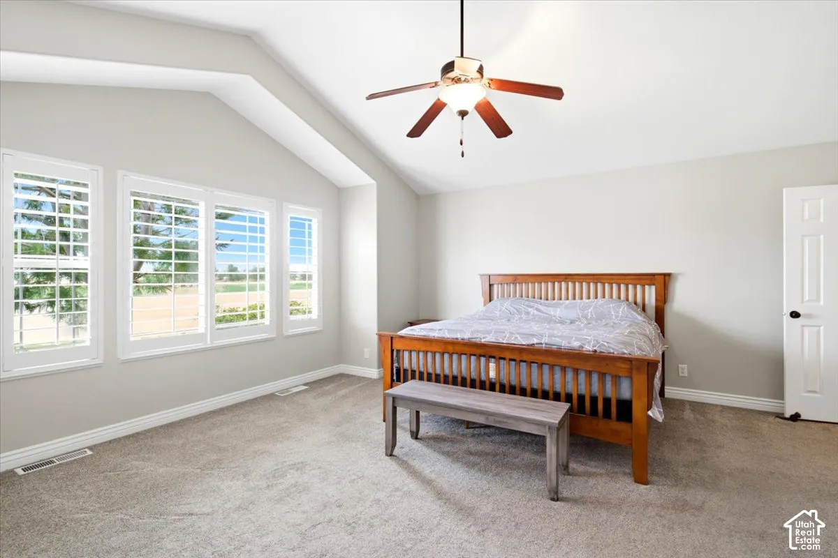 Vaulted ceiling with ceiling fan, light gray wall paint, and light-colored carpet flooring