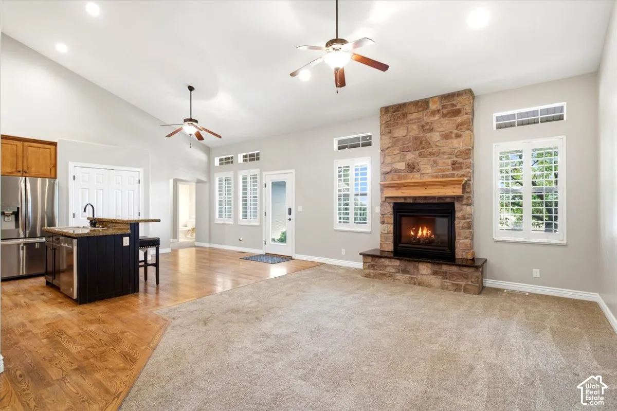 Stone-clad fireplace with a wood mantle, vaulted ceiling with recessed lighting, wood-finish flooring, and a kitchen island with a built-in sink