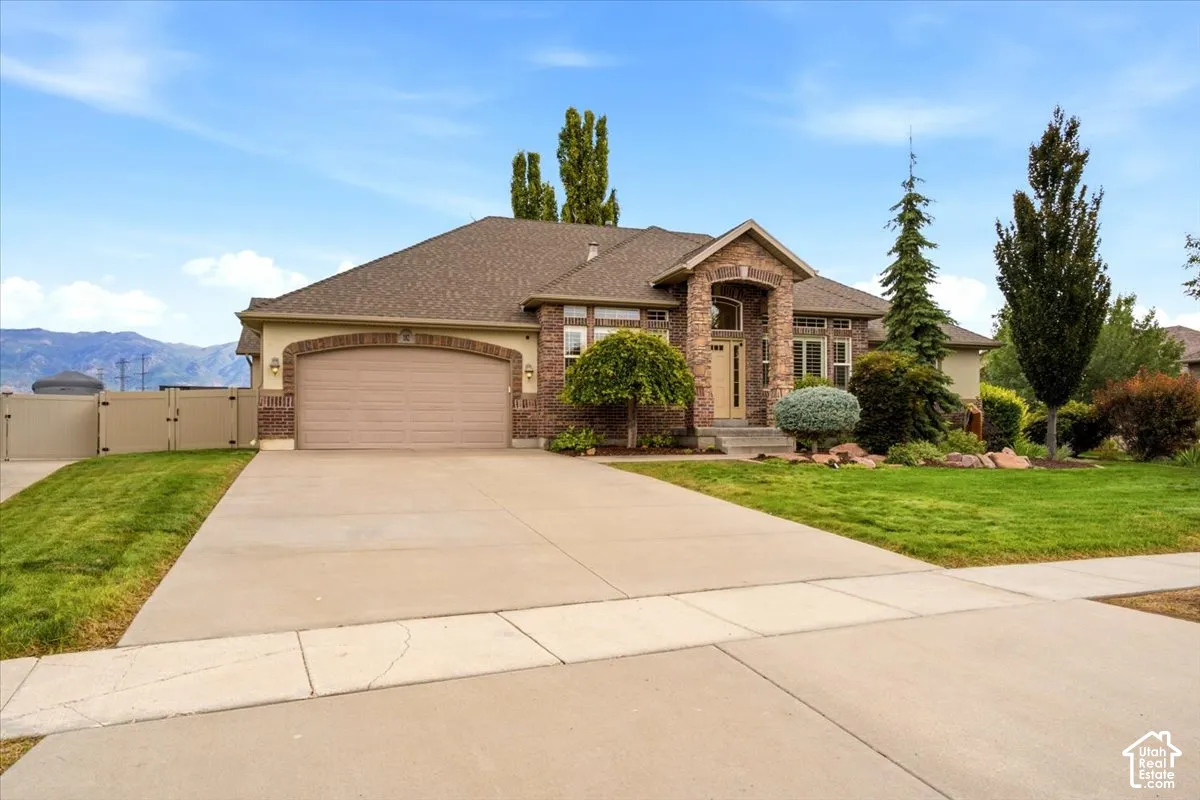 Brick and stone facade with an arched entry, mature landscaping, paved driveway, and an attached garage