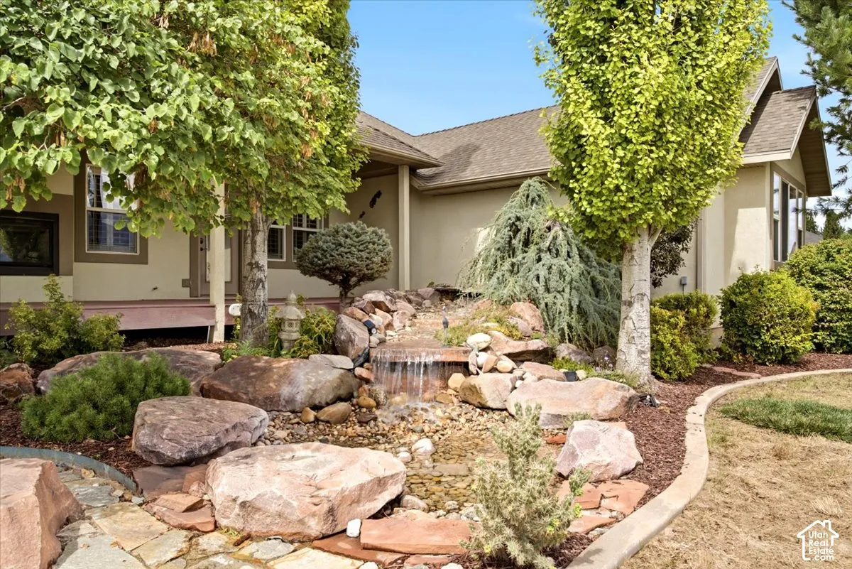 Landscaped yard featuring a rock waterfall, mature trees, and a flagstone pathway