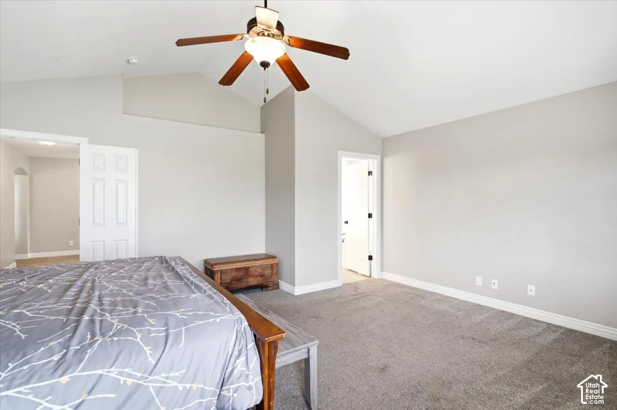 Master bedroom with vaulted ceiling, a ceiling fan, light gray wall paint, gray carpet flooring, and white trim