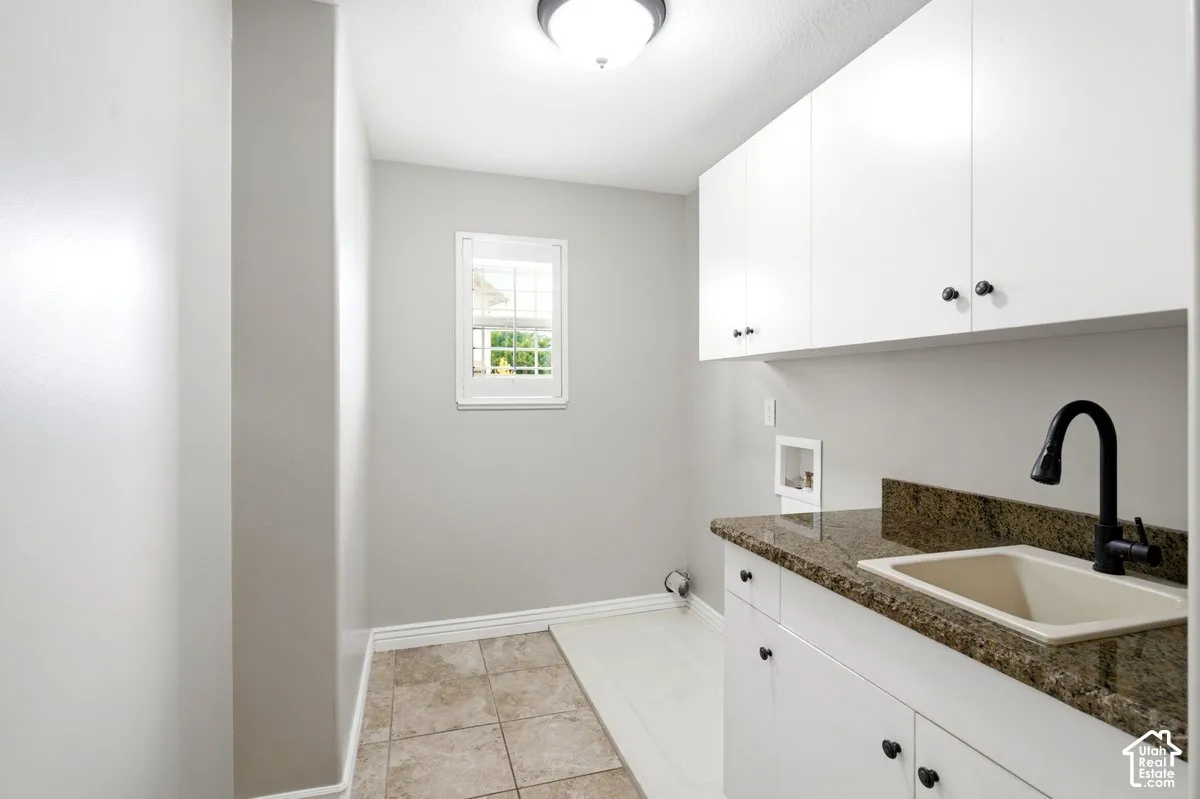 White cabinetry with dark hardware, stone-finish countertop with integrated sink, matte black faucet, and tile flooring