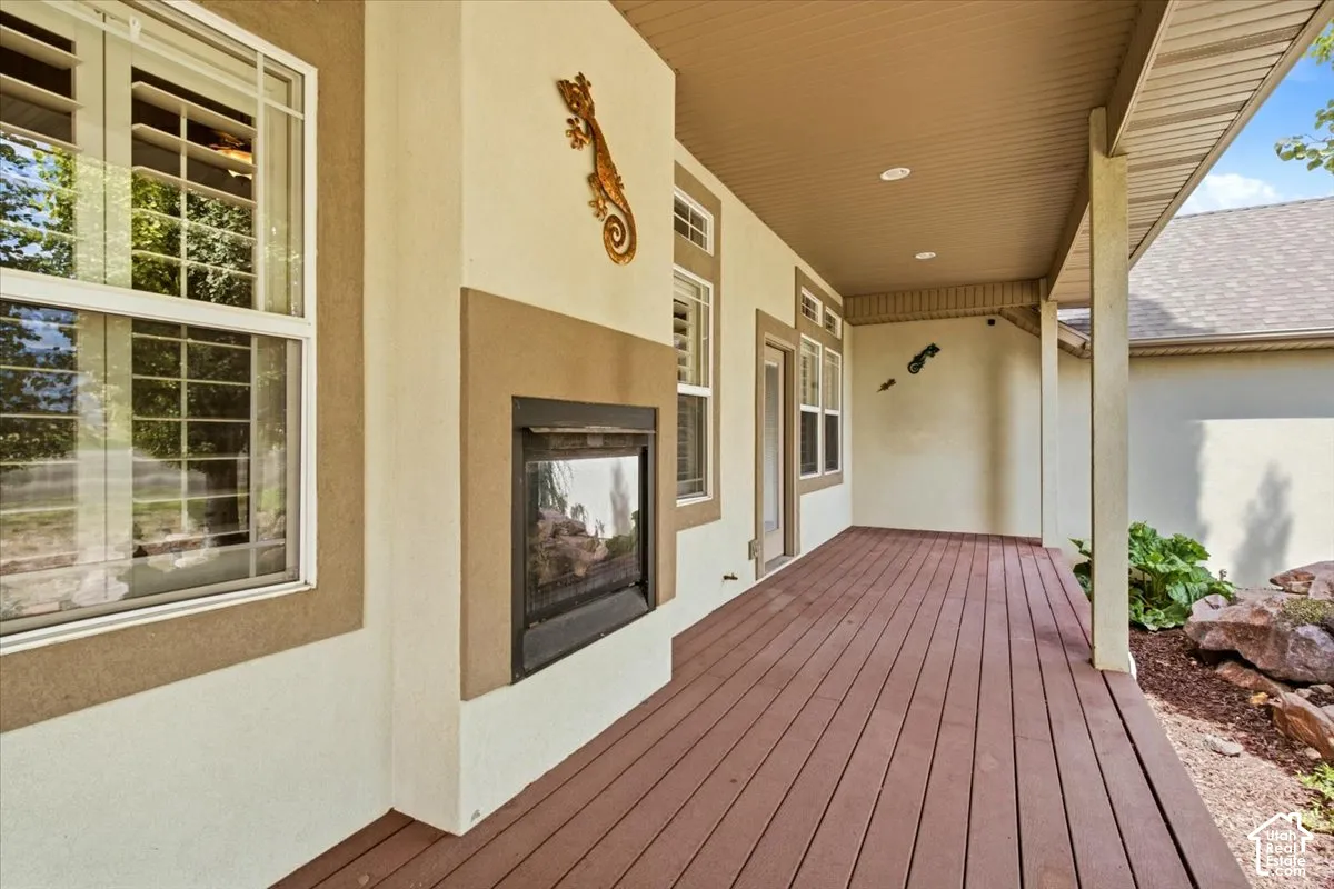 Covered porch with wood-finish decking, stucco exterior, and an outdoor fireplace
