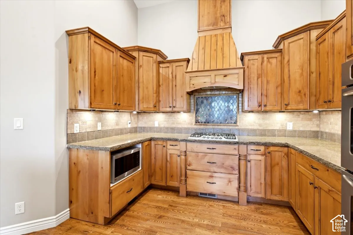 Kitchen with wood-finish cabinetry, granite-style countertops, mosaic tile backsplash, built-in microwave, and stainless steel gas range