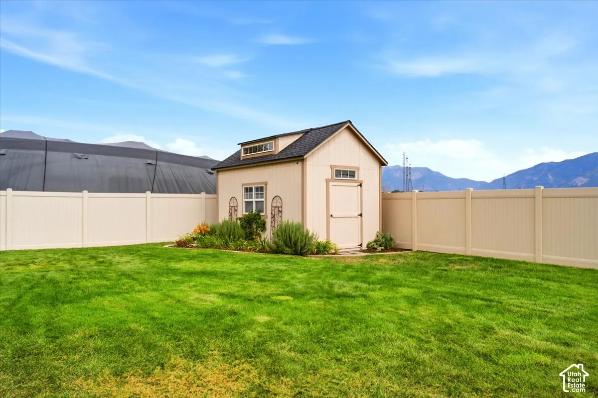 Expansive green lawn with a privacy fence, featuring a storage shed with a dormer window and an adjacent garden bed