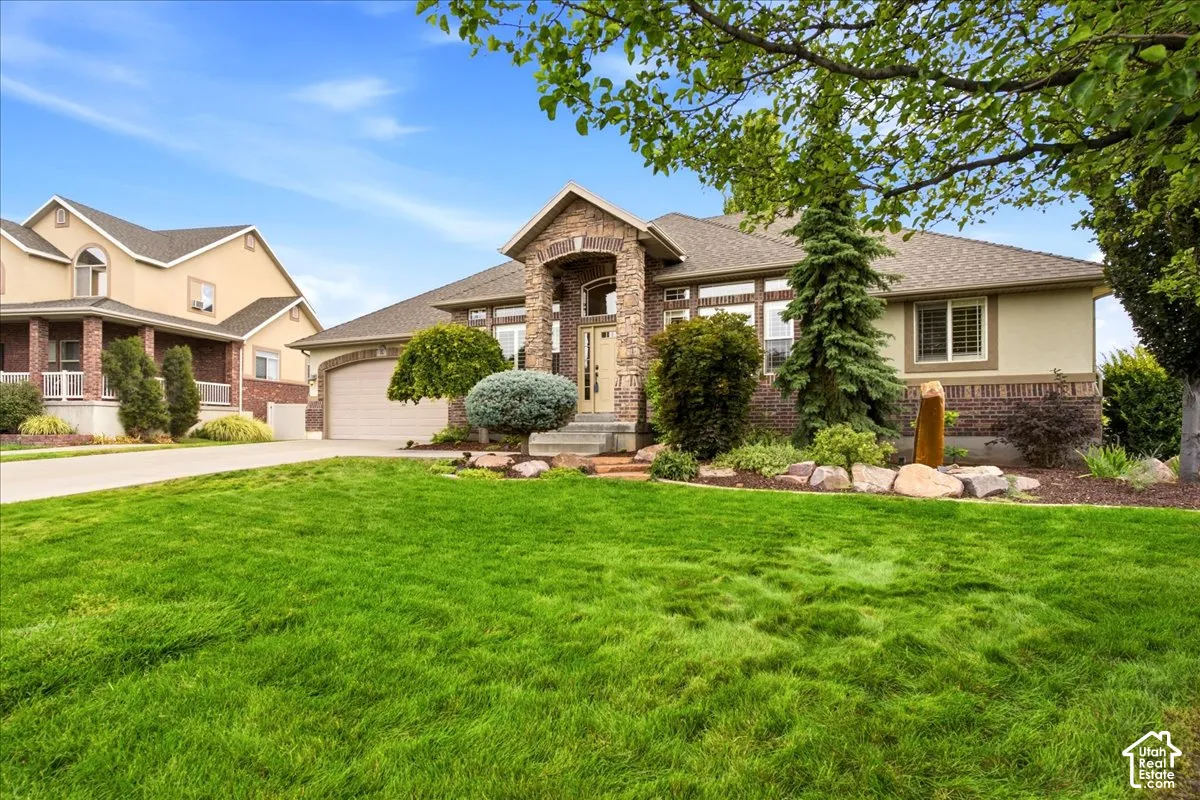 Stone and stucco exterior, arched entry, integrated garage, manicured front lawn, and established landscaping