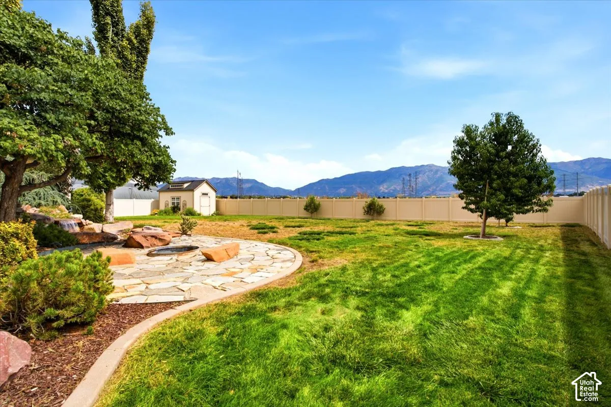 Expansive backyard featuring a stone fire pit area, a water feature, a manicured lawn, and a storage shed
