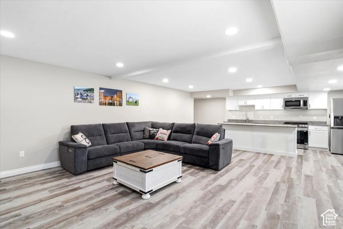 Wood-finish flooring, recessed lighting, white perimeter cabinetry, stainless steel appliances, and a stone-finish countertop