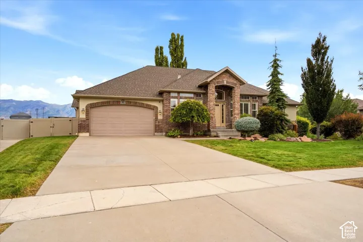 Brick and stone facade with an arched entry, mature landscaping, paved driveway, and an attached garage