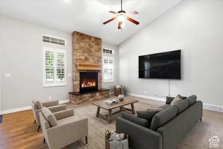 Vaulted ceilings, floor-to-ceiling stone fireplace with a wood mantel, transom windows, and a ceiling fan