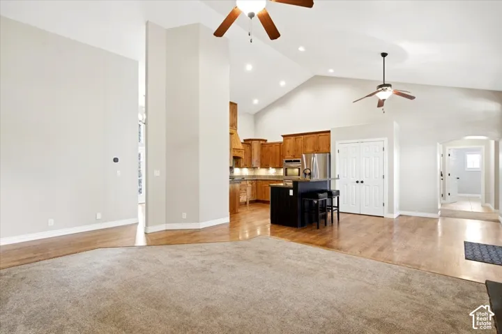 Vaulted ceiling with recessed lighting, wood-finish flooring, wood cabinetry, stainless steel appliances, and a built-in kitchen island