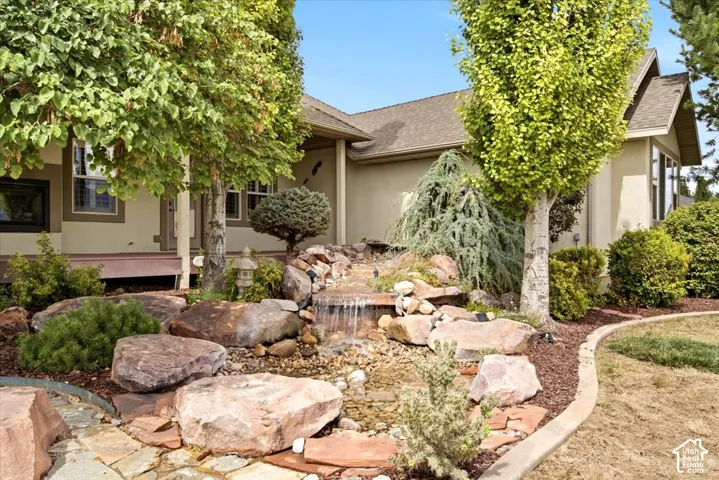 Landscaped yard featuring a rock waterfall, mature trees, and a flagstone pathway