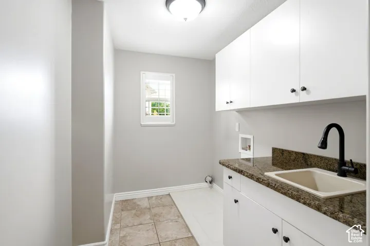 White cabinetry with dark hardware, stone-finish countertop with integrated sink, matte black faucet, and tile flooring