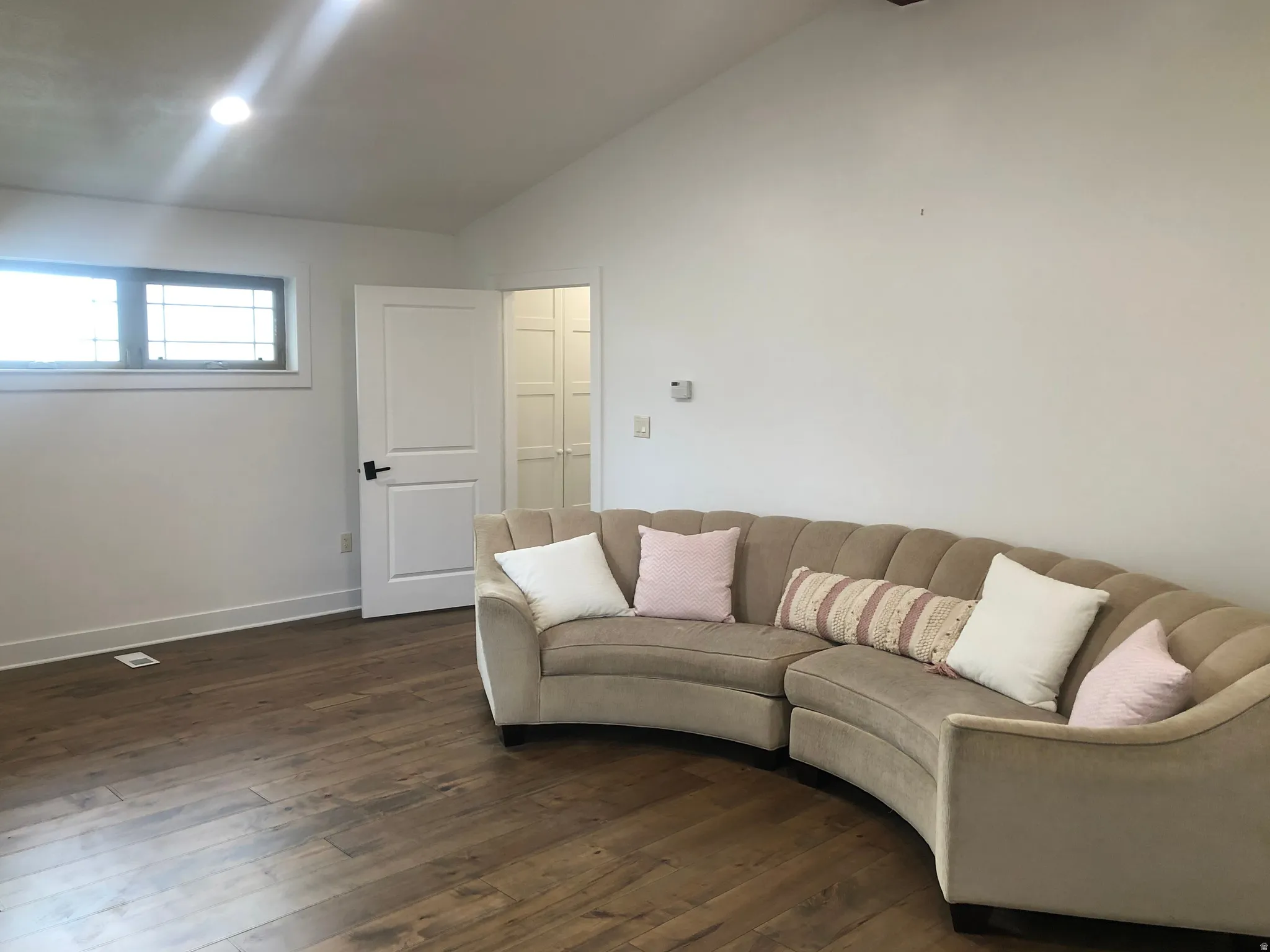 Wood-finish flooring, white walls, vaulted ceiling, recessed lighting, and a window with dark trim