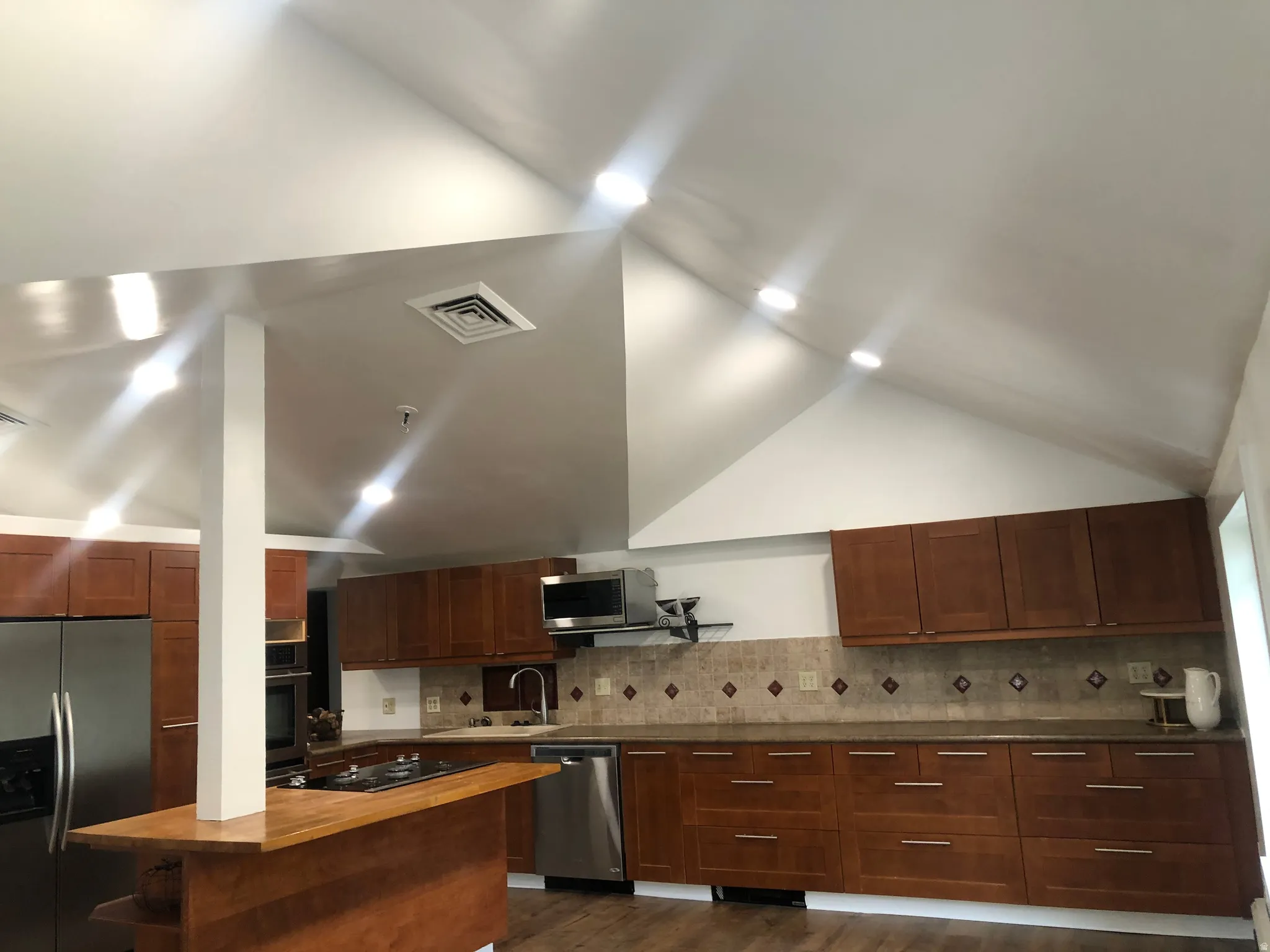 Kitchen featuring vaulted ceilings, recessed lighting, wood-finish cabinetry, stainless steel appliances, and a tile backsplash