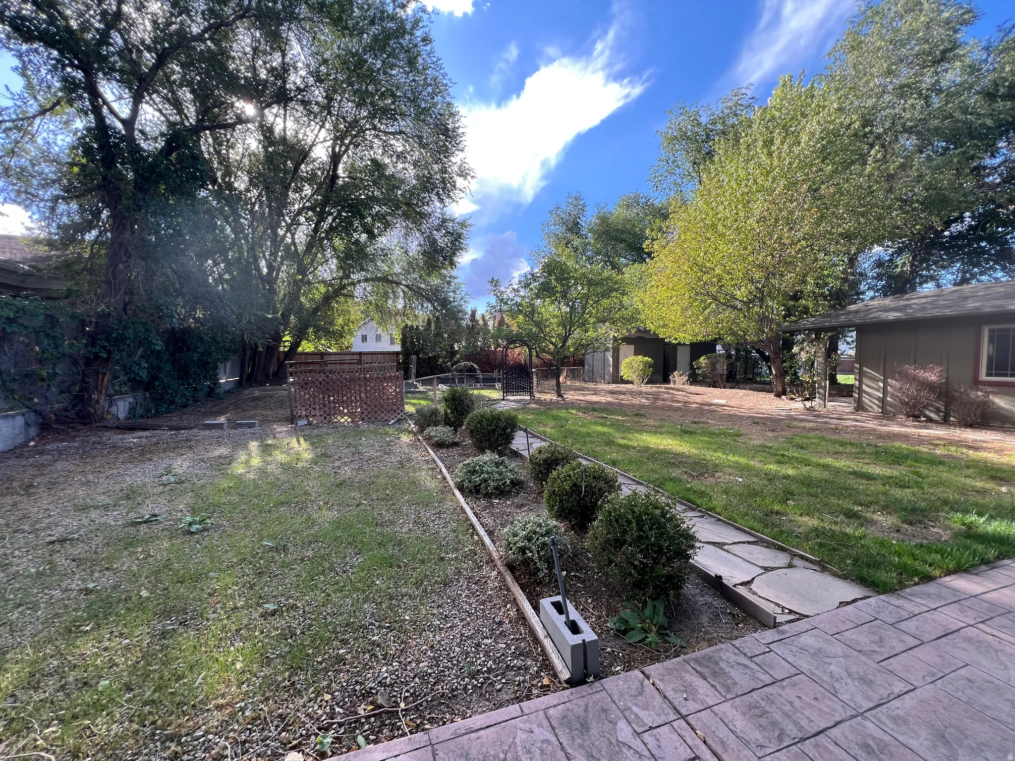 Expansive backyard featuring mature trees, a stamped concrete patio, a stone pathway, and well-defined garden beds with shrubbery