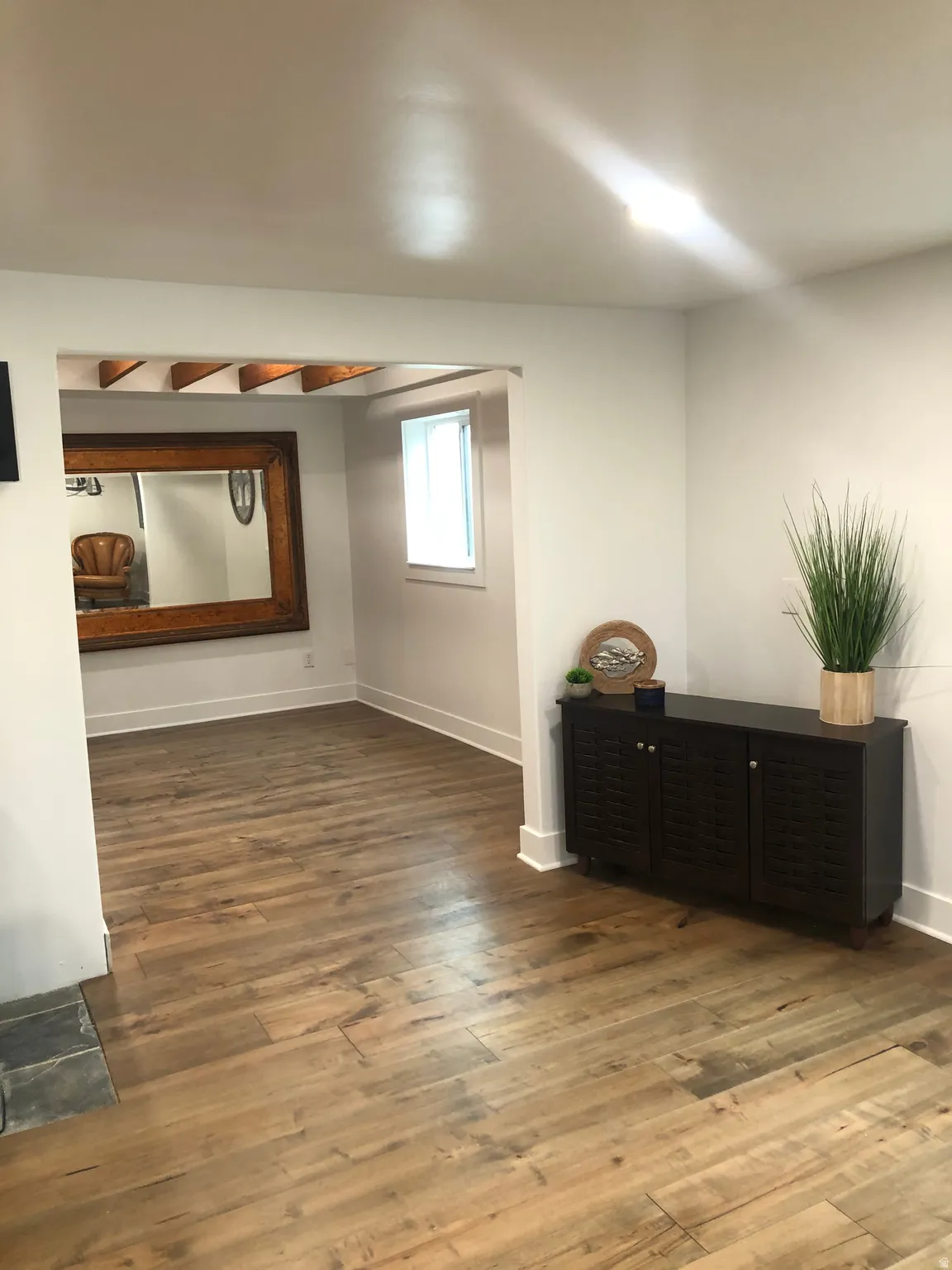 Wood-finish flooring throughout, white baseboards, recessed ceiling lighting, and a window providing natural illumination