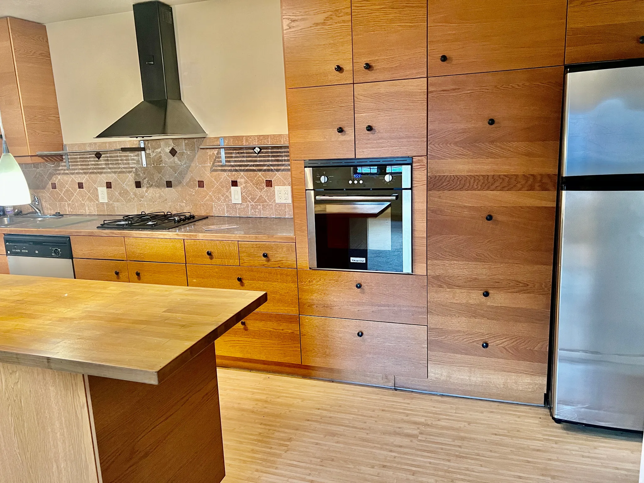 Kitchen featuring wood cabinetry, integrated wall oven, stainless steel refrigerator, and a gas cooktop