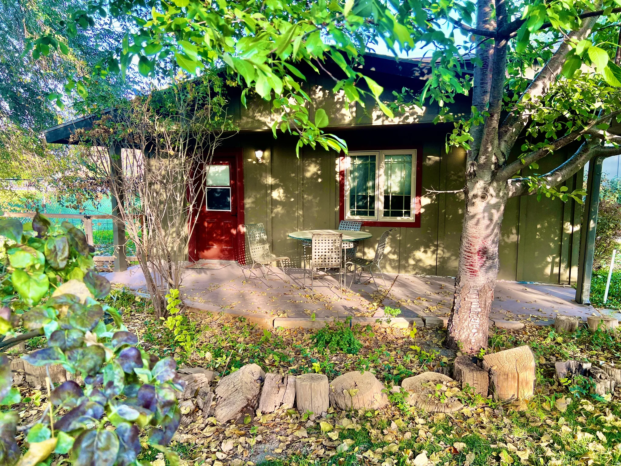 Exterior siding, red entry door, white-framed window, concrete patio, and garden landscaping