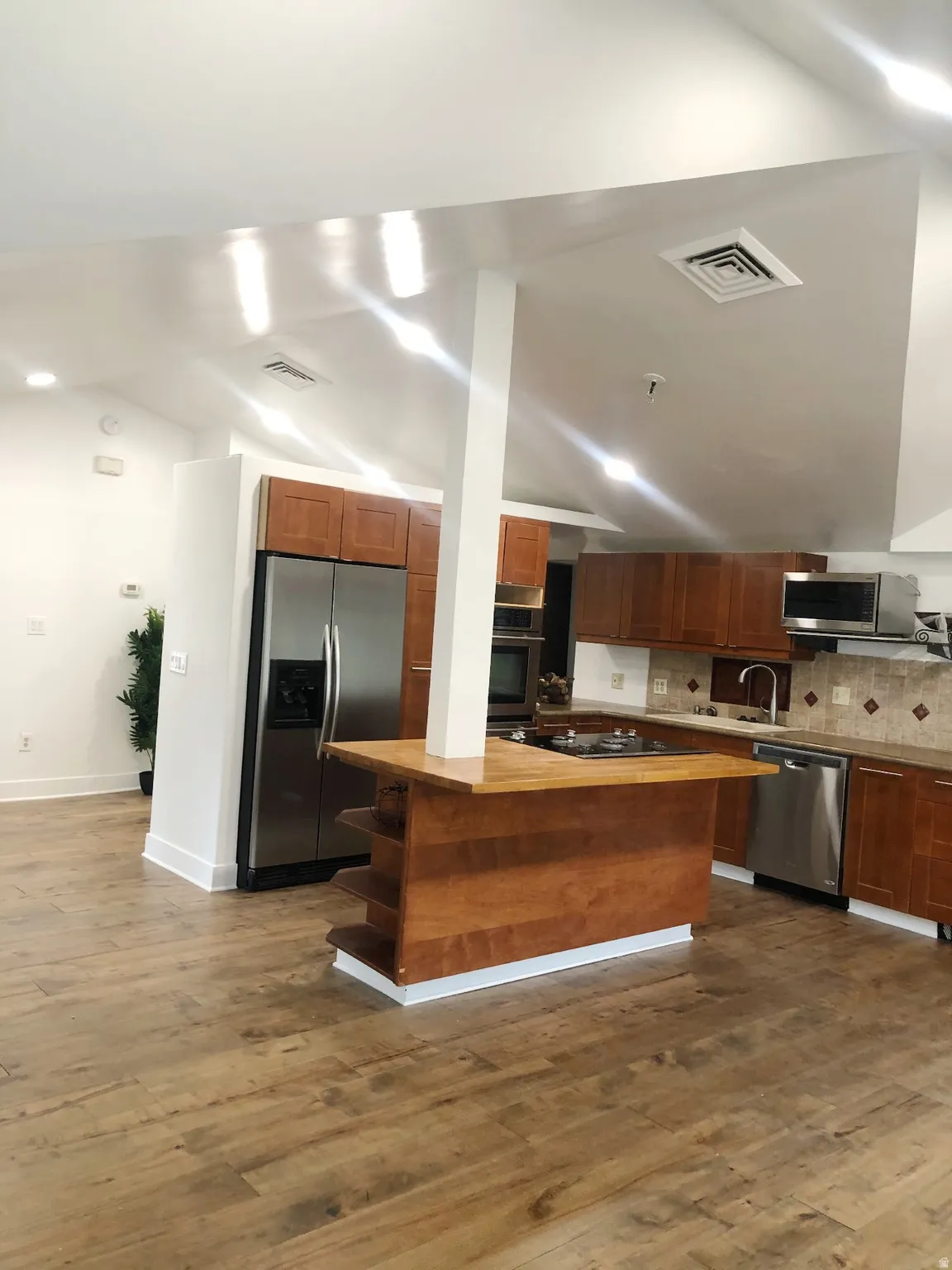 Vaulted ceilings with recessed lighting, wood-finish flooring, wood cabinetry, stainless steel appliances, and a built-in island with shelving