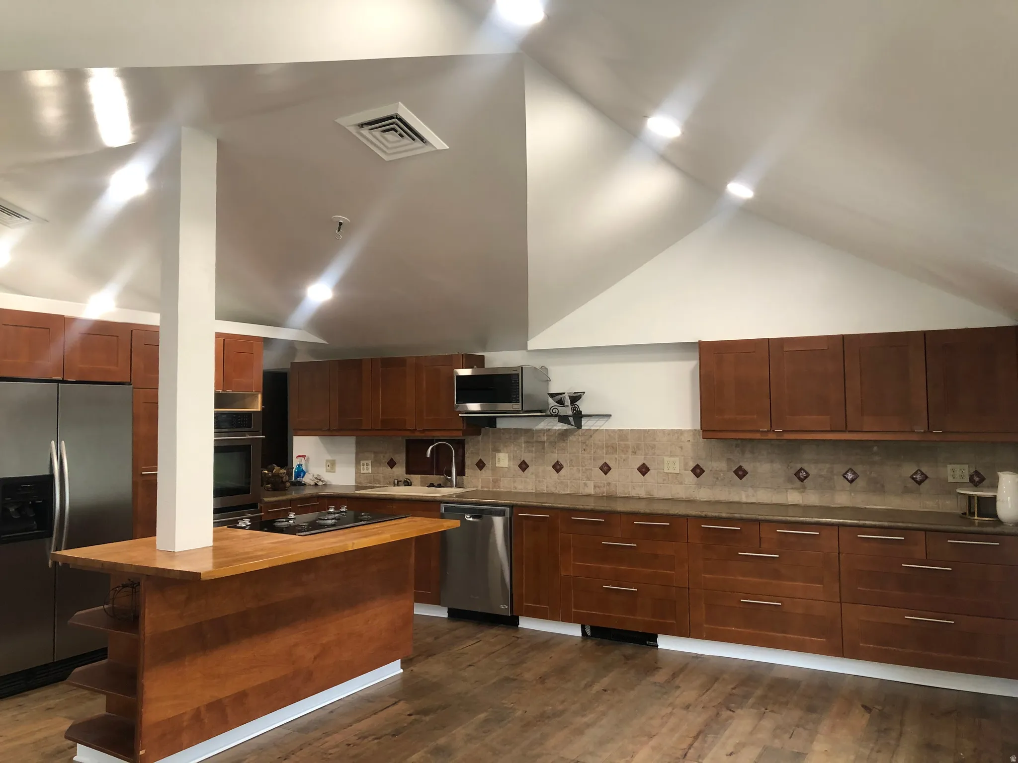 Kitchen featuring wood-finish flooring, abundant wood cabinetry, stainless steel appliances, and a tiled backsplash