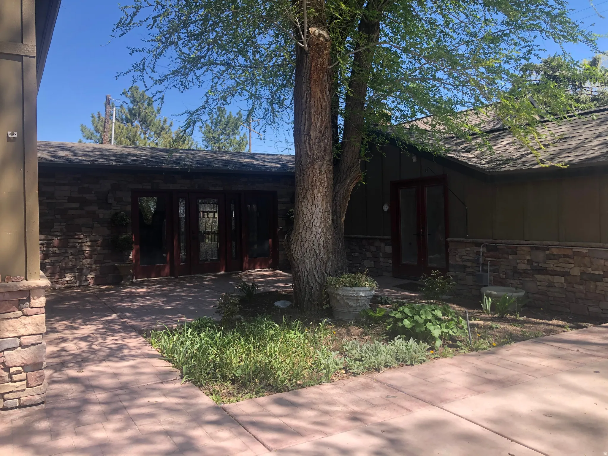 Courtyard entrance, stone veneer facade, dark-framed French doors, wood-paneled exterior, covered patio, mature tree