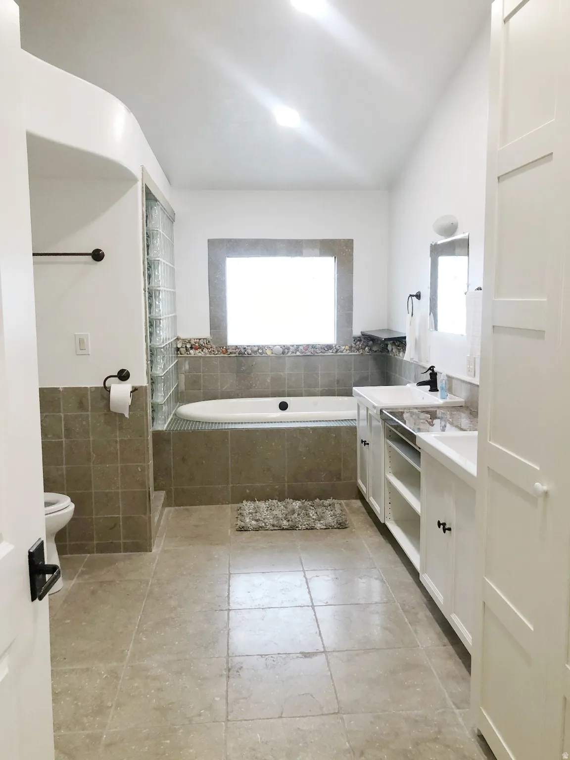Tile flooring, freestanding bathtub, dual vanity with undermount sinks, built-in cabinetry, and a walk-in shower with glass block enclosure