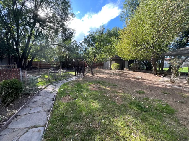 Expansive backyard with a stone-paver pathway, mature trees, and fenced perimeter