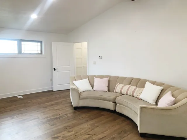 Vaulted ceiling, recessed lighting, wood-finish flooring, white paneled door with black hardware, and horizontal windows