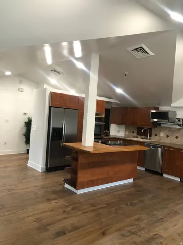 Kitchen featuring wood-finish flooring, stainless steel appliances, wood cabinetry, and an island with a built-in cooktop
