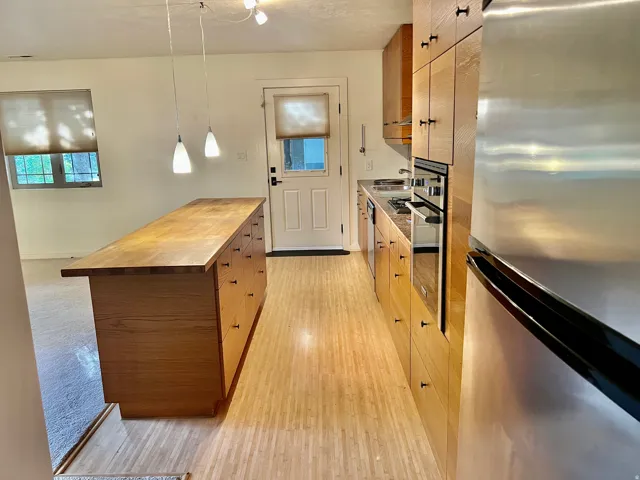 Kitchen featuring wood-finish cabinetry, stainless steel appliances, a center island with integrated storage, and light-tone flooring