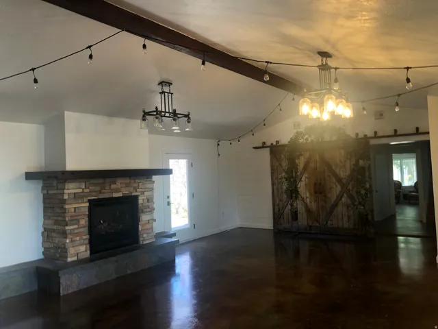 Spacious open-concept living area featuring a brick fireplace with dark hearth, dark wood-finish flooring, exposed beam ceiling detail, and track lighting throughout