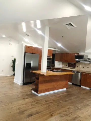Vaulted ceilings with recessed lighting, wood-finish flooring, wood cabinetry, stainless steel appliances, and a built-in island with shelving