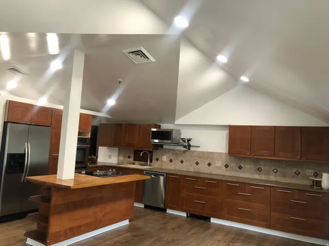 Vaulted ceiling with recessed lighting, wood-finish flooring, stainless steel appliances, wood cabinetry, and a kitchen island with built-in cooktop