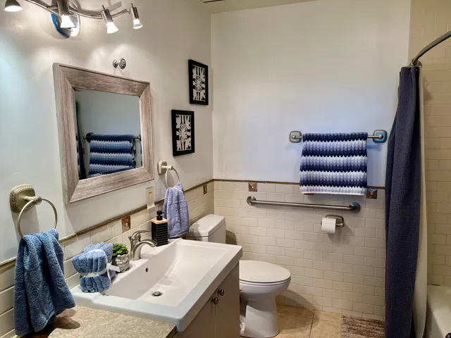 Bathroom featuring a vanity with an integrated sink, framed mirror, track lighting, subway tile wainscoting, and a built-in grab bar