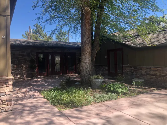 Courtyard entrance, stone veneer facade, dark-framed French doors, wood-paneled exterior, covered patio, mature tree