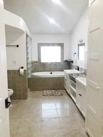 Tile flooring, freestanding bathtub, dual vanity with undermount sinks, built-in cabinetry, and a walk-in shower with glass block enclosure