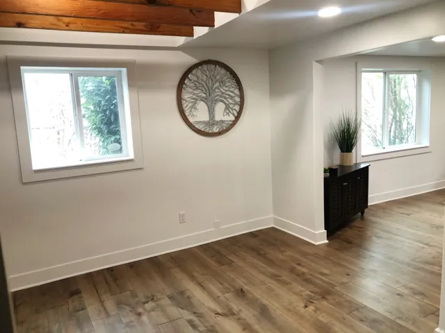 Wood-finish flooring, recessed ceiling lighting, exposed wood beams, white trim, and light-filled windows