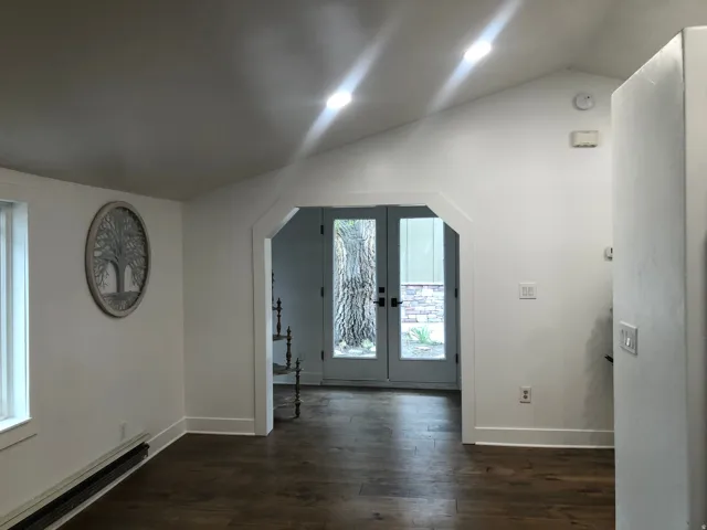 Vaulted ceiling with recessed lighting, wood-finish flooring, white walls, and French doors