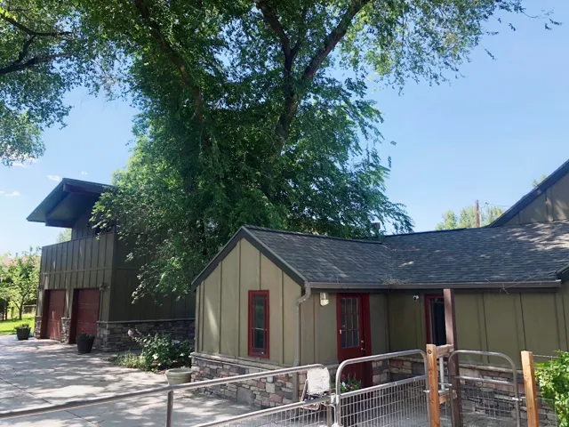 Exterior siding with stone-finish wainscoting, asphalt shingle roofing, and red-trimmed entry doors