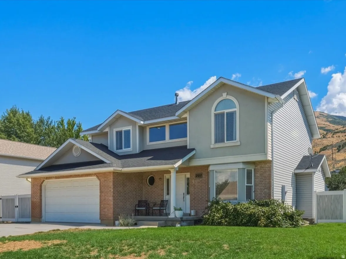 Two-story residence with brick and siding exterior, integrated two-car garage, front-facing arched window, and a fenced backyard