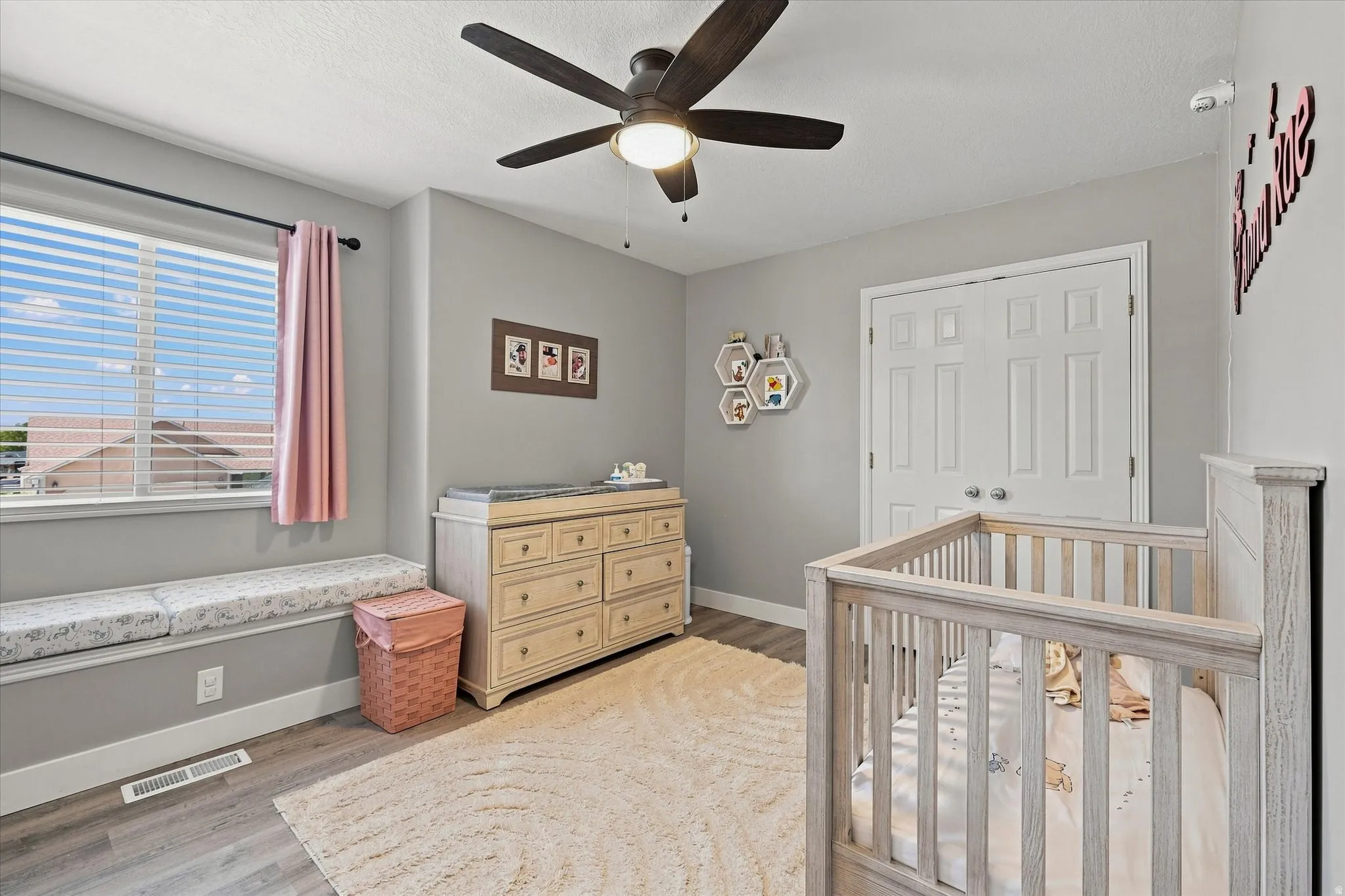Window bench seating, wood-finish flooring, ceiling fan with light fixture, and double-door closet